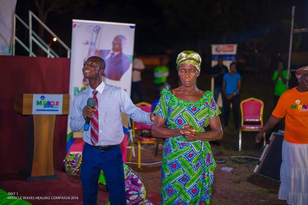 An elderly woman standing still as she is prayed for